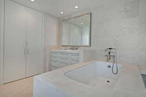 Bathroom with vanity, a washtub, and tile walls