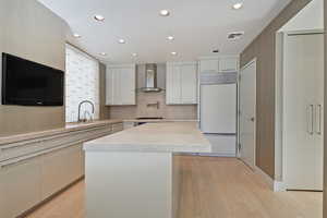 Kitchen featuring light hardwood / wood-style flooring, wall chimney exhaust hood, white cabinets, built in refrigerator, and a kitchen island