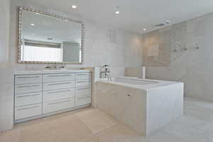 Bathroom featuring a tub to relax in, vanity, and tile walls