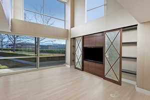 Unfurnished living room featuring light wood-type flooring, a towering ceiling, and a wealth of natural light