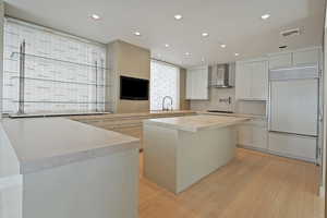 Kitchen with built in refrigerator, a center island, stovetop, wall chimney range hood, and white cabinetry