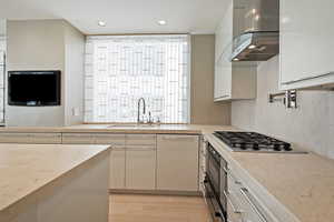 Kitchen with sink, light wood-type flooring, stainless steel gas cooktop, and island range hood