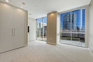 Unfurnished bedroom with light colored carpet, a wall of windows, and access to outside