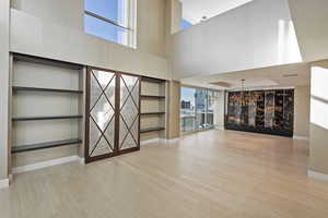 Unfurnished living room with built in shelves, light hardwood / wood-style flooring, and a towering ceiling