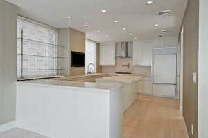 Kitchen with wall chimney exhaust hood, white cabinetry, kitchen peninsula, and paneled built in fridge