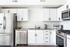 Kitchen featuring decorative backsplash, sink, white cabinetry, stainless steel appliances, and dark hardwood / wood-style flooring