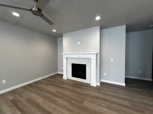 Unfurnished living room featuring ceiling fan, a brick fireplace, and dark hardwood / wood-style floors