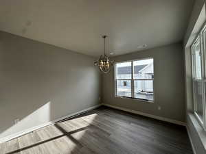 Unfurnished room with hardwood / wood-style flooring and a notable chandelier