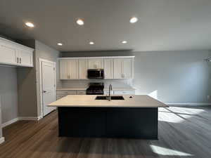 Kitchen with white cabinetry, stainless steel appliances, sink, dark hardwood / wood-style floors, and a kitchen island with sink