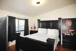 Bedroom with a textured ceiling, vaulted ceiling, and dark hardwood / wood-style flooring