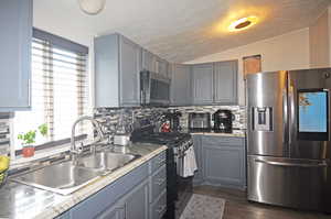 Kitchen featuring sink, gray cabinets, decorative backsplash, lofted ceiling, and stainless steel appliances