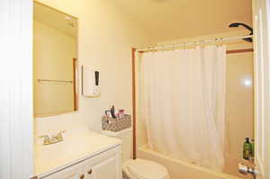 Full bathroom with toilet, vanity, shower / bathtub combination with curtain, and vaulted ceiling