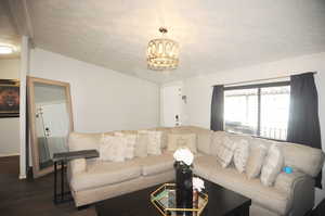 Living room with a textured ceiling, dark hardwood / wood-style flooring, and an inviting chandelier