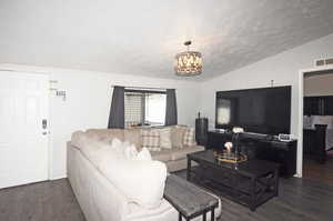 Living room with vaulted ceiling, an inviting chandelier, and dark hardwood / wood-style flooring