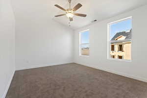 Spare room with ceiling fan, lofted ceiling, and dark colored carpet