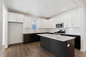 Kitchen with appliances with stainless steel finishes, white cabinetry, sink, a kitchen island, and dark hardwood / wood-style flooring