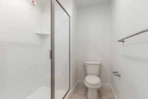 Bathroom with toilet, walk in shower, and tile patterned flooring