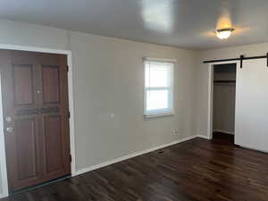 Unfurnished bedroom with dark wood-type flooring, a closet, and a barn door