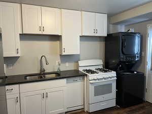 Kitchen featuring dark hardwood / wood-style flooring, sink, white cabinetry, white appliances, and stacked washer / drying machine