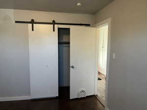 Unfurnished bedroom featuring dark wood-type flooring, a closet, and a barn door