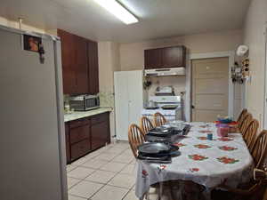 Kitchen with backsplash, white appliances, dark brown cabinets, and light tile patterned flooring