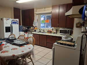 Kitchen featuring dark brown cabinets, sink, tasteful backsplash, light tile patterned floors, and white appliances