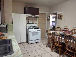 Kitchen with light tile patterned floors, sink, dark brown cabinetry, and white range with gas cooktop