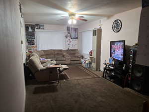 Carpeted living room featuring ceiling fan and a textured ceiling