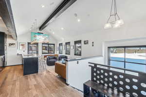 Kitchen with decorative light fixtures, vaulted ceiling with beams, an island with sink, sink, and light hardwood / wood-style flooring