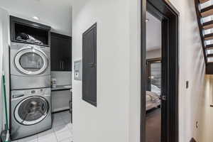 Clothes washing area with cabinets, stacked washer / dryer, light tile patterned floors, and electric panel