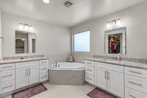 Bathroom featuring tiled bath, a textured ceiling, vanity, and tile patterned flooring