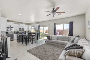 Living room with a textured ceiling, light tile patterned floors, and ceiling fan