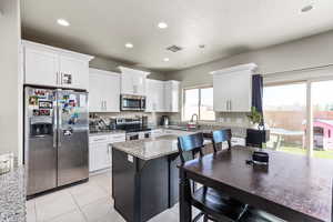 Kitchen with white cabinetry, light tile patterned floors, a kitchen island, stainless steel appliances, and light stone counters