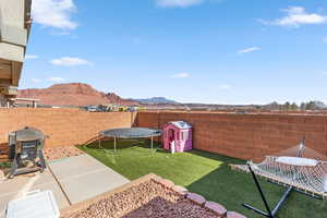 View of yard featuring a mountain view, a patio, a trampoline, and a shed