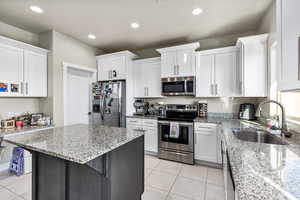 Kitchen with a kitchen breakfast bar, sink, white cabinets, light stone counters, and stainless steel appliances