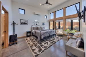 Bedroom featuring ceiling fan, a towering ceiling, concrete flooring, and a wall mounted air conditioner