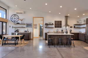 Kitchen with dark brown cabinetry, a center island, a wall mounted air conditioner, wall chimney range hood, and a kitchen breakfast bar