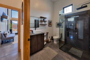 Bathroom with concrete flooring, a shower with door, toilet, and plenty of natural light