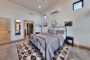 Bedroom featuring a wall unit AC, concrete flooring, and a high ceiling