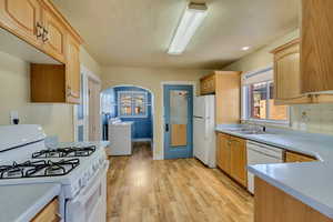 Kitchen with sink, white appliances, light hardwood / wood-style flooring, and light brown cabinets