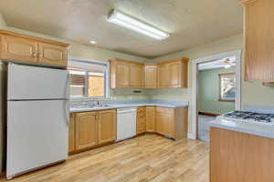 Kitchen with white appliances, sink, light wood-type flooring, backsplash, and light brown cabinets