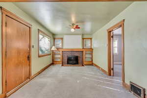 Unfurnished living room with a brick fireplace, light carpet, and ceiling fan