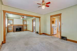 Unfurnished living room with a fireplace, light colored carpet, and ceiling fan