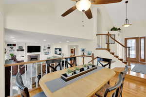 Dining area with a towering ceiling, built in shelves, ceiling fan, light hardwood / wood-style flooring, and a tiled fireplace