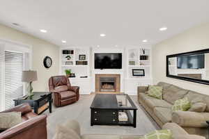 Living room with a fireplace, built in features, and light colored carpet