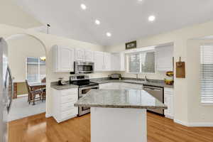 Kitchen featuring white cabinets, appliances with stainless steel finishes, a center island, sink, and light stone counters