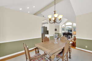 Dining area with light wood-type flooring, vaulted ceiling with beams, and an inviting chandelier