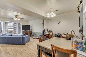 Dining room with ceiling fan with notable chandelier, ornamental molding, and light wood-type flooring