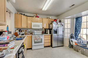 Kitchen featuring sink, light brown cabinets, white appliances, and a textured ceiling