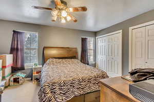 Carpeted bedroom with multiple closets, a textured ceiling, and ceiling fan